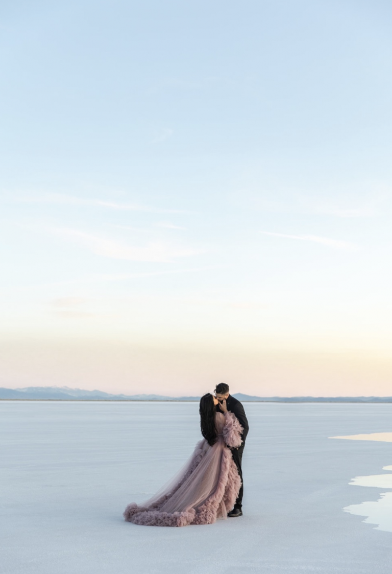 A woman in a elegant gown embraces her fiancé during their dreamy Bonneville Salt Flats engagement session photographed by Kyla Jeanette Photography.