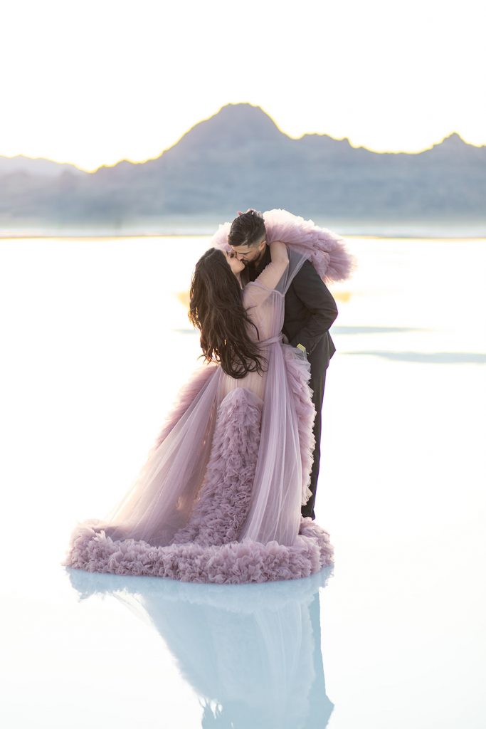 A woman in a elegant gown embraces her fiancé during their dreamy Bonneville Salt Flats engagement session photographed by Kyla Jeanette Photography.
