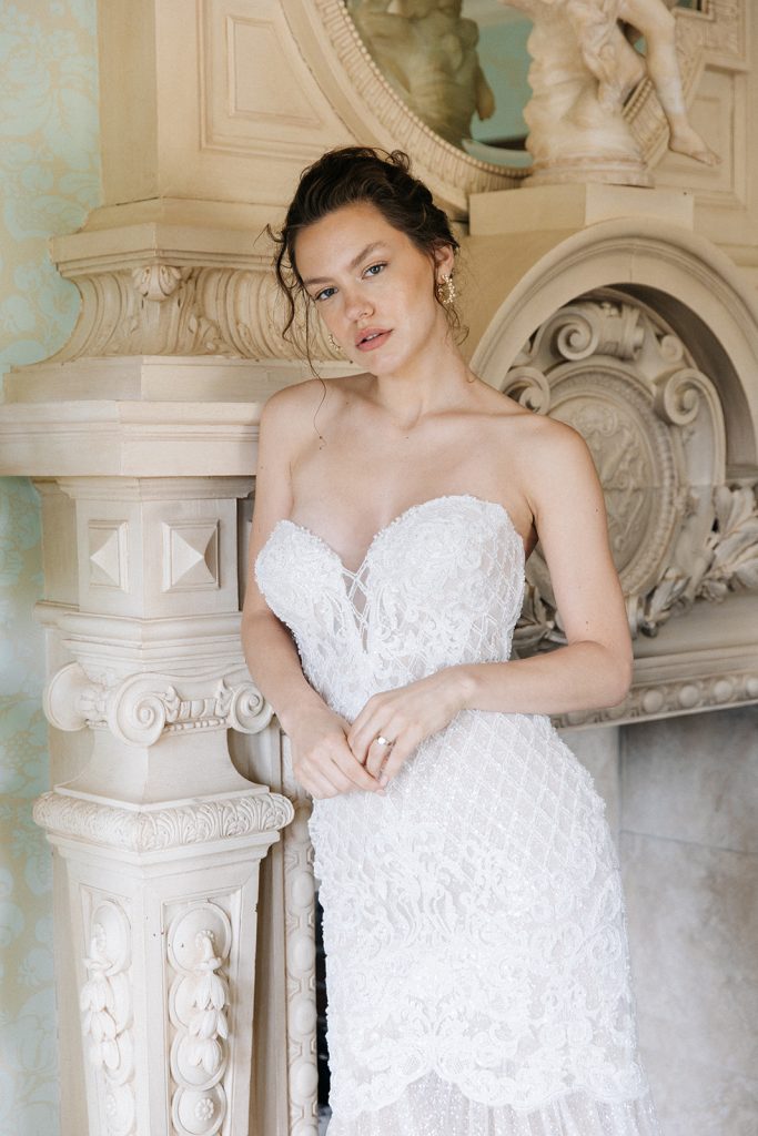 A bride poses while resting against an ornate fireplace during her editorial wedding by Kyla Jeanette