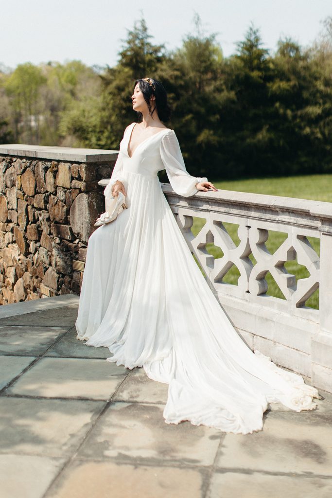 An elegantly dressed bride poses against a cement patio during her editorial wedding