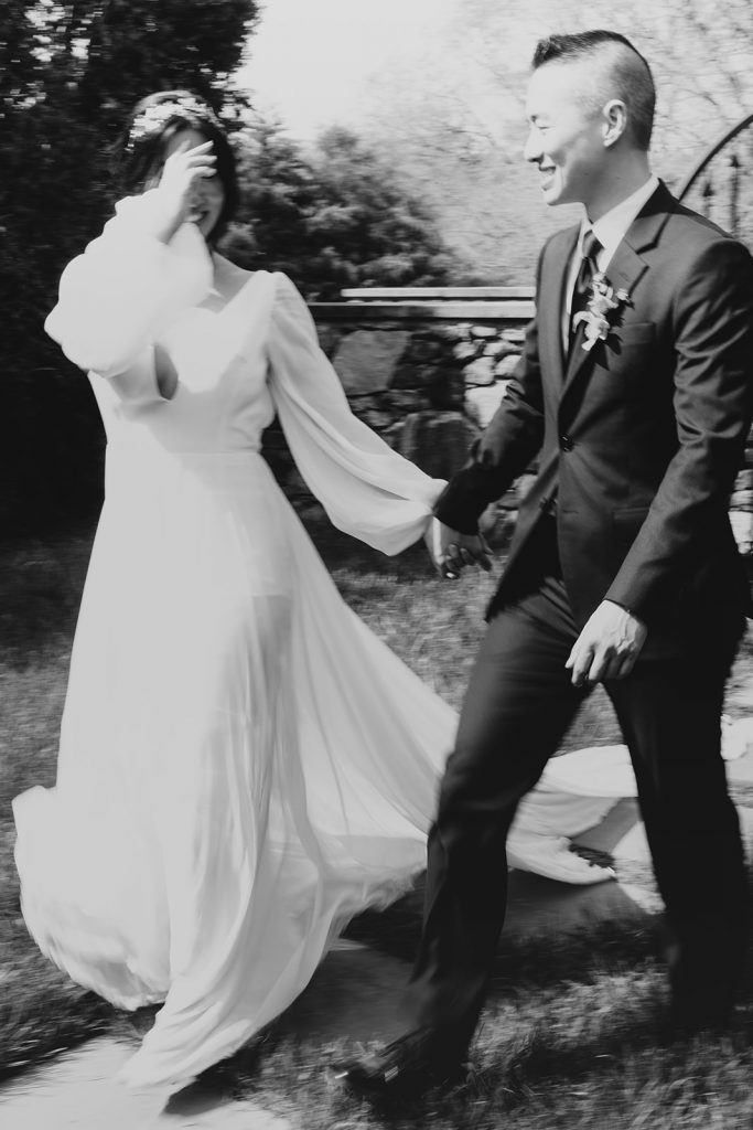 Black and white photo of bride and groom holding hands and smiling bashfully