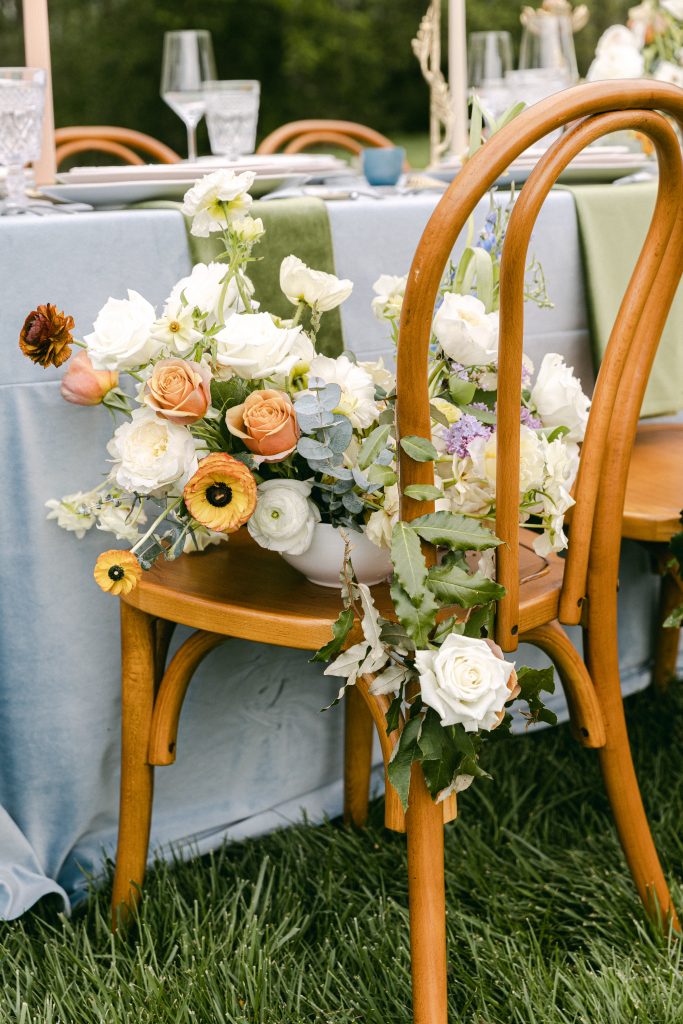 Green and blue table set-up with a floral arrangement laid set on a brown wooden chair, taken by Kyla Jeanette Photography