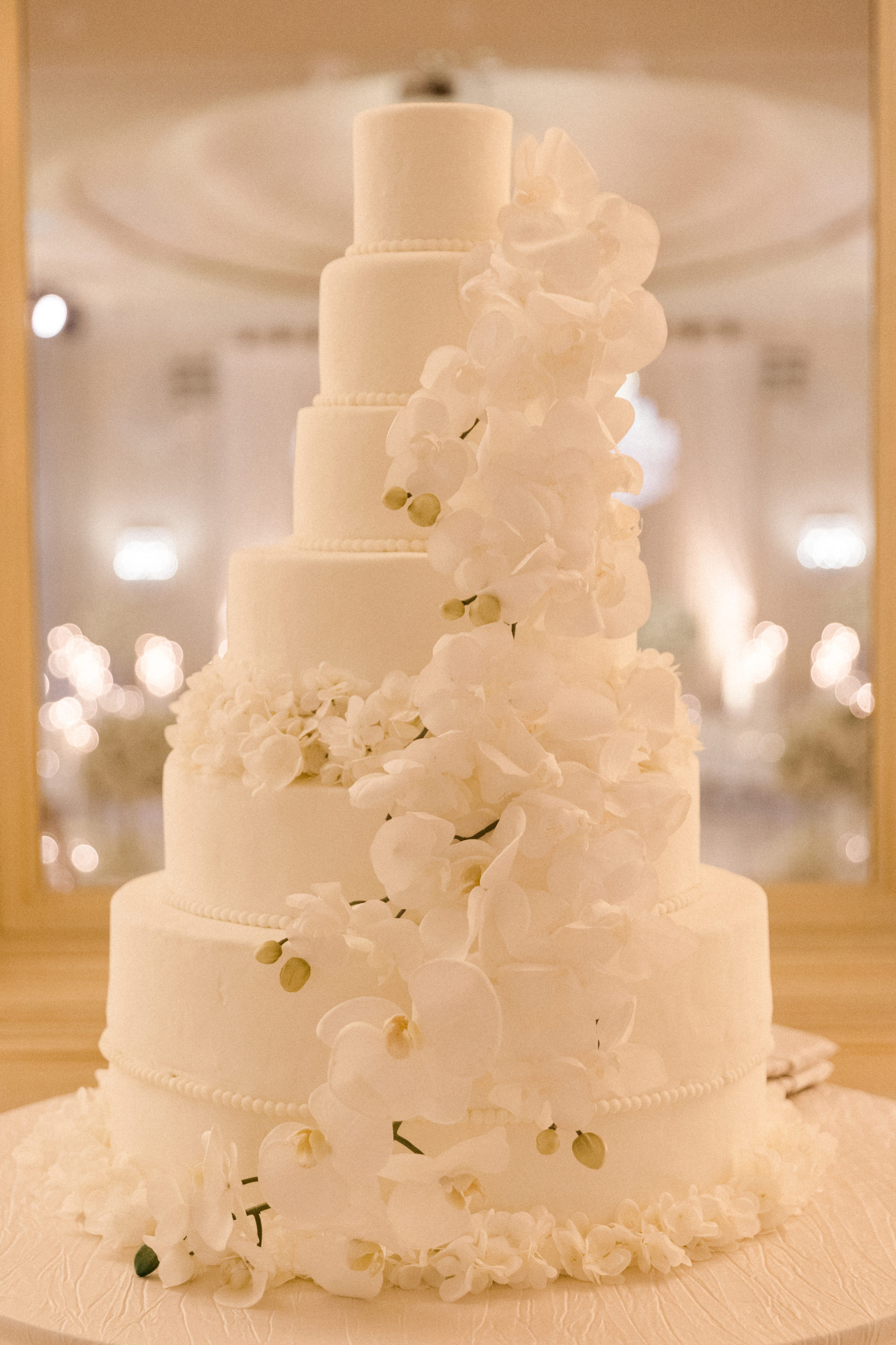 Six-layered white decorative wedding cake with floral orchid decorations on it that gives off an elegant and luxurious vibe