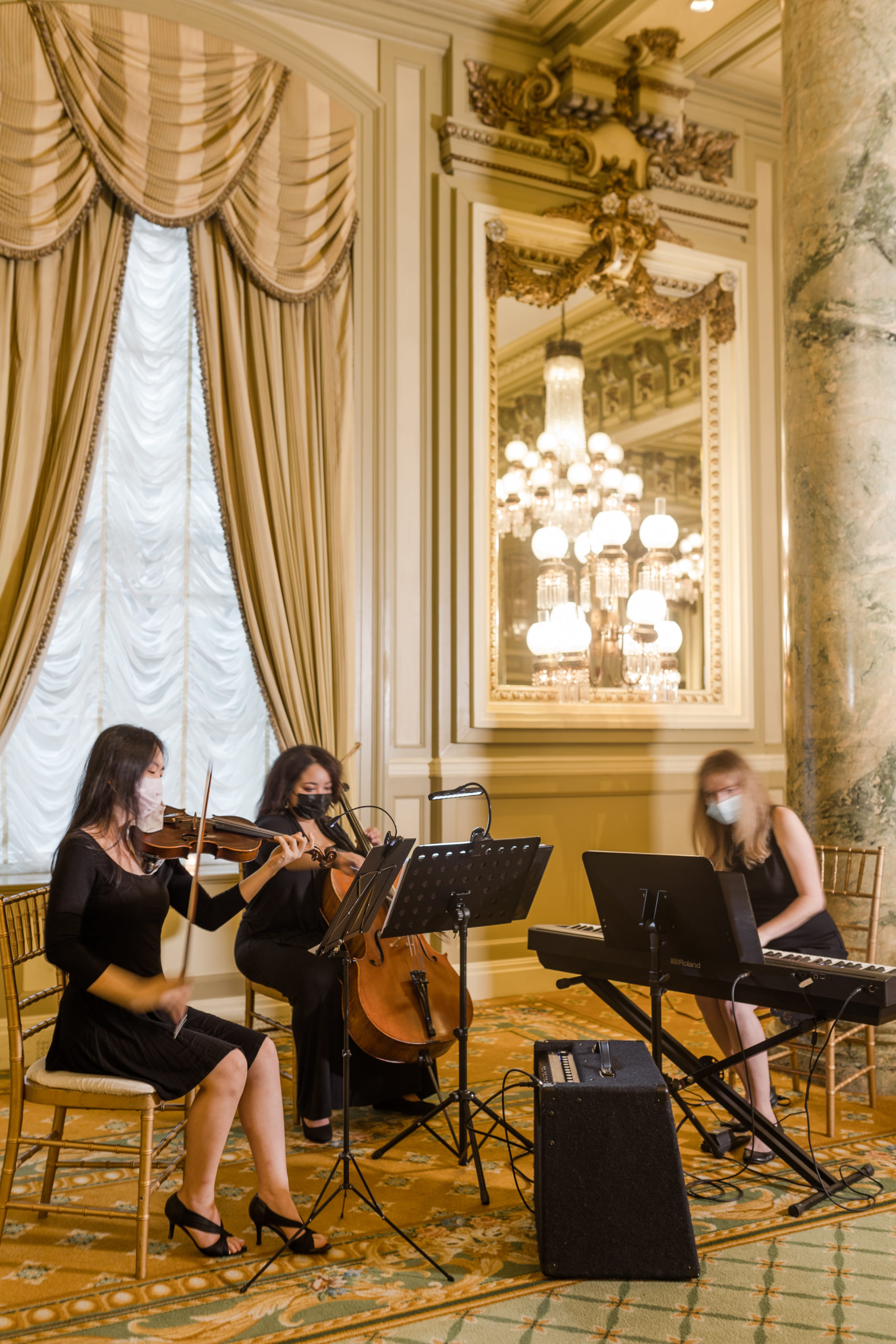 Three women playing their own instruments, including a violin, a cello, and a keyboard piano during a luxurious wedding reception
