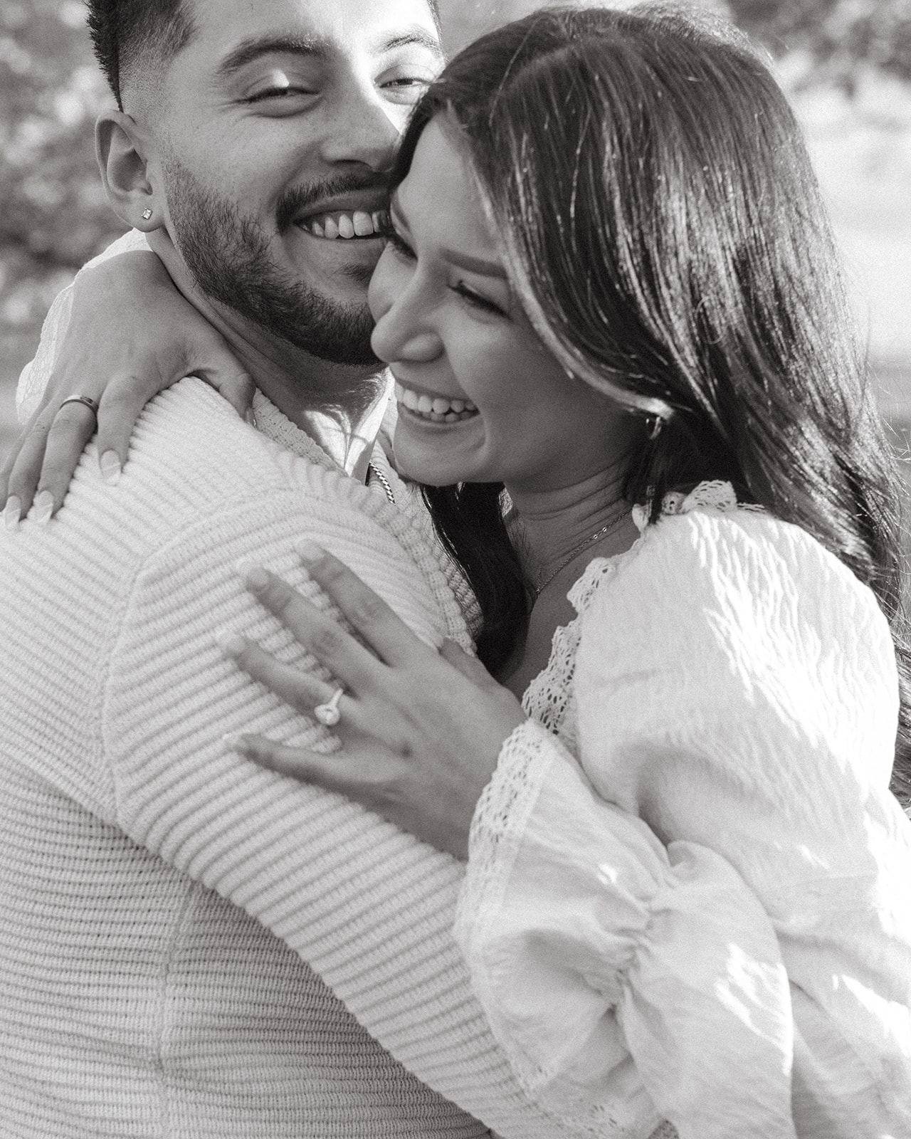 Black and white photo of bride and groom wrapping their arms around each other, showing the bride's ring on her finger