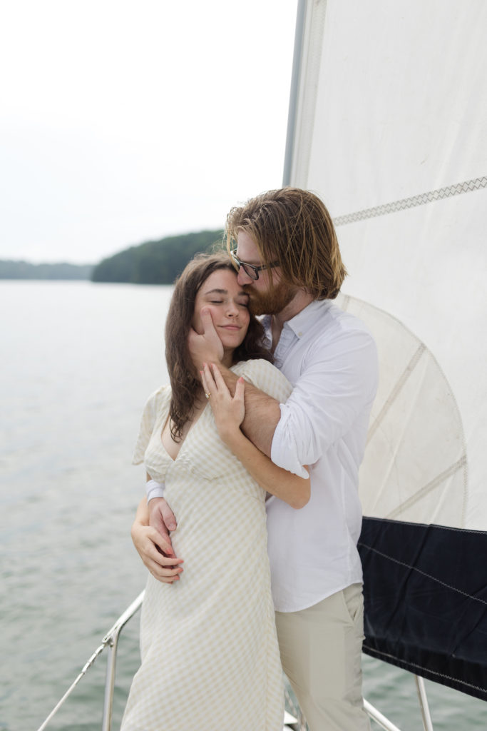 Ethereal Sailboat Engagement Photos in Atlanta, Georgia: Guy plants a kiss on his fiance's forehead as he hugs her from behind, taken by Kyla Jeanette